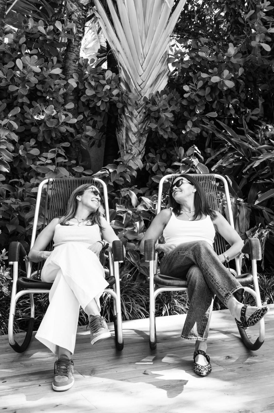 Two women sitting in chairs outdoors with plants in the background